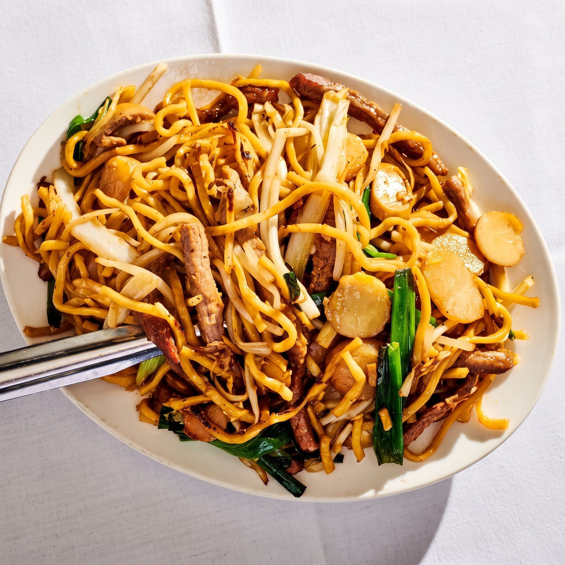 Stir-fried noodles with bean sprouts, vegetables, and chopsticks on a white plate.