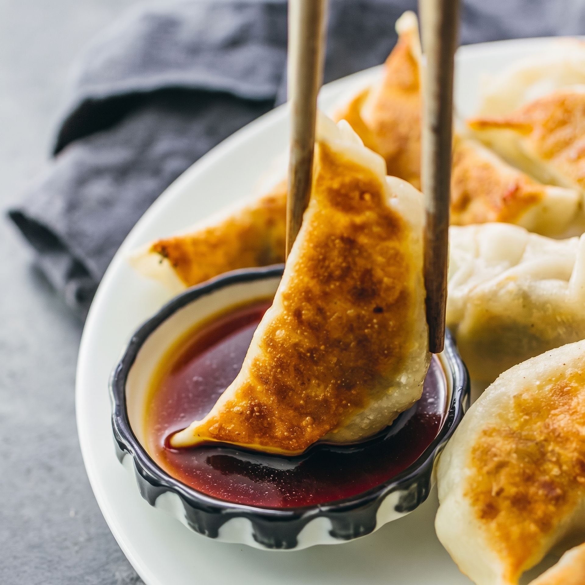 Dumpling being dipped in soy sauce with chopsticks on a white plate