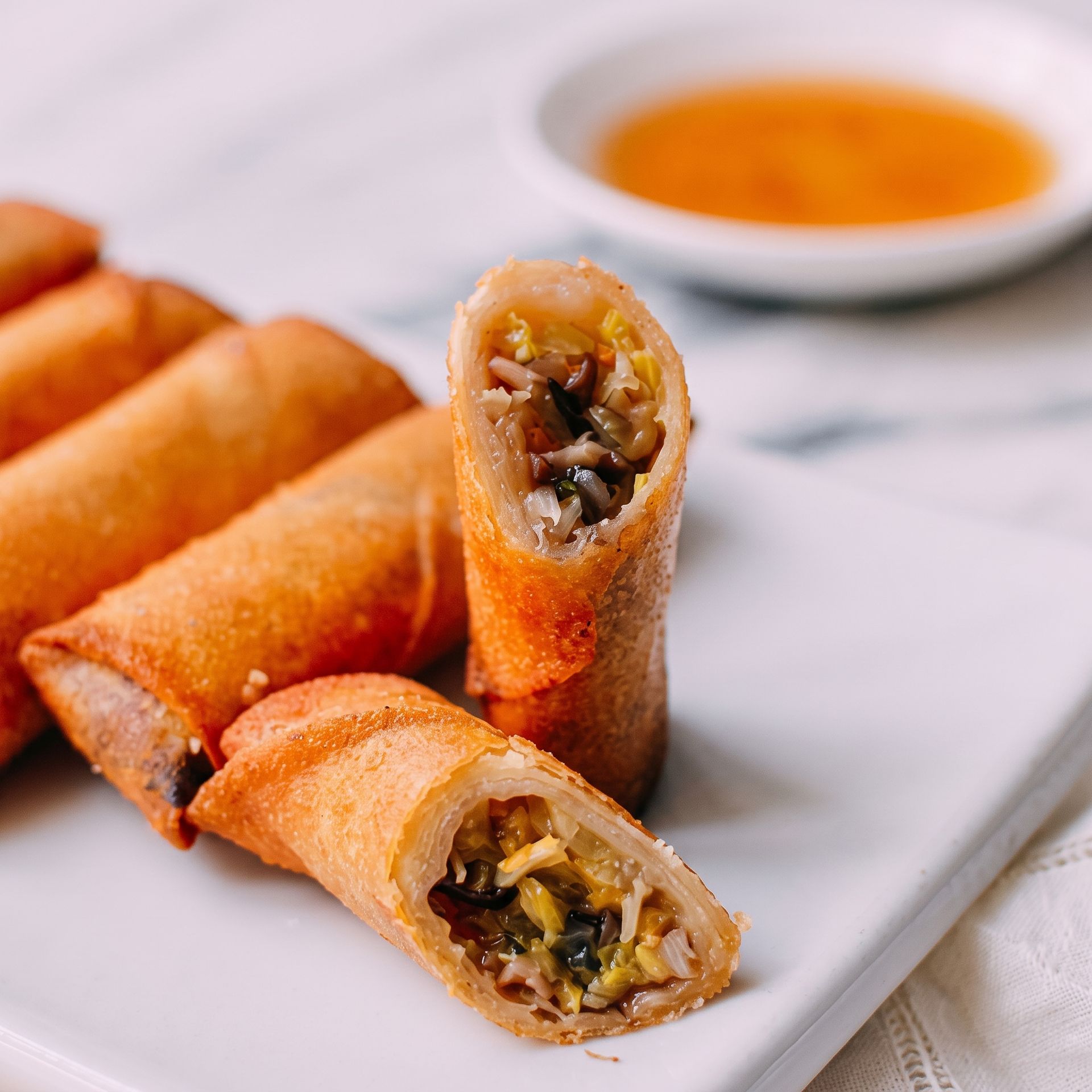 Crispy spring rolls on a white plate with a dipping sauce in the background