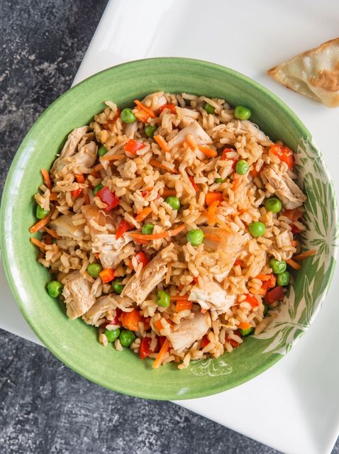 Green bowl of fried rice with chicken and vegetables on a white tray
