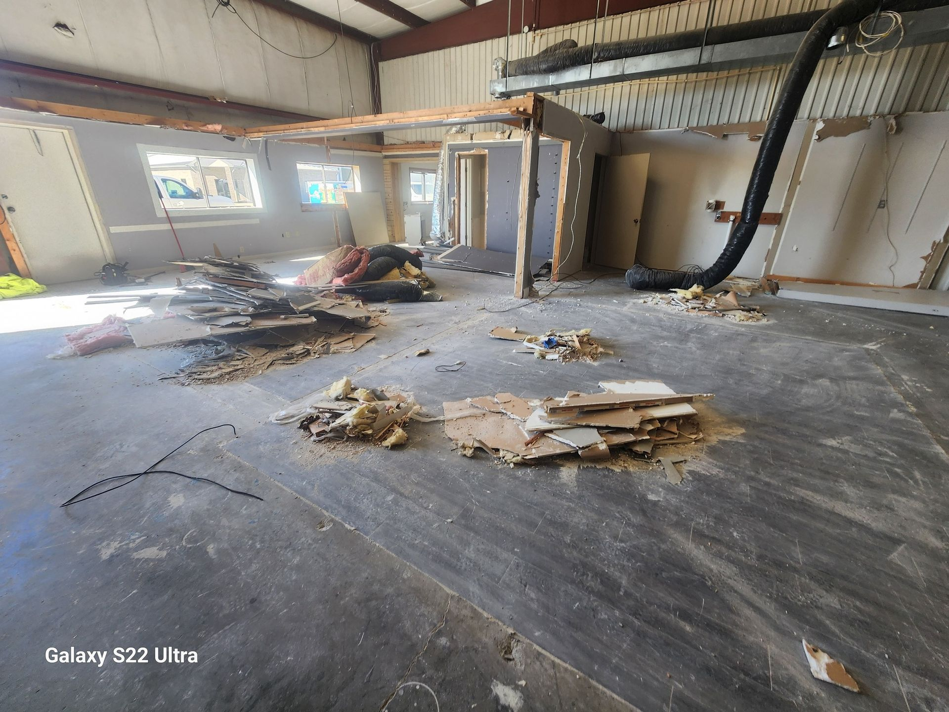 Damaged warehouse interior with debris scattered across a concrete floor and open bay doors