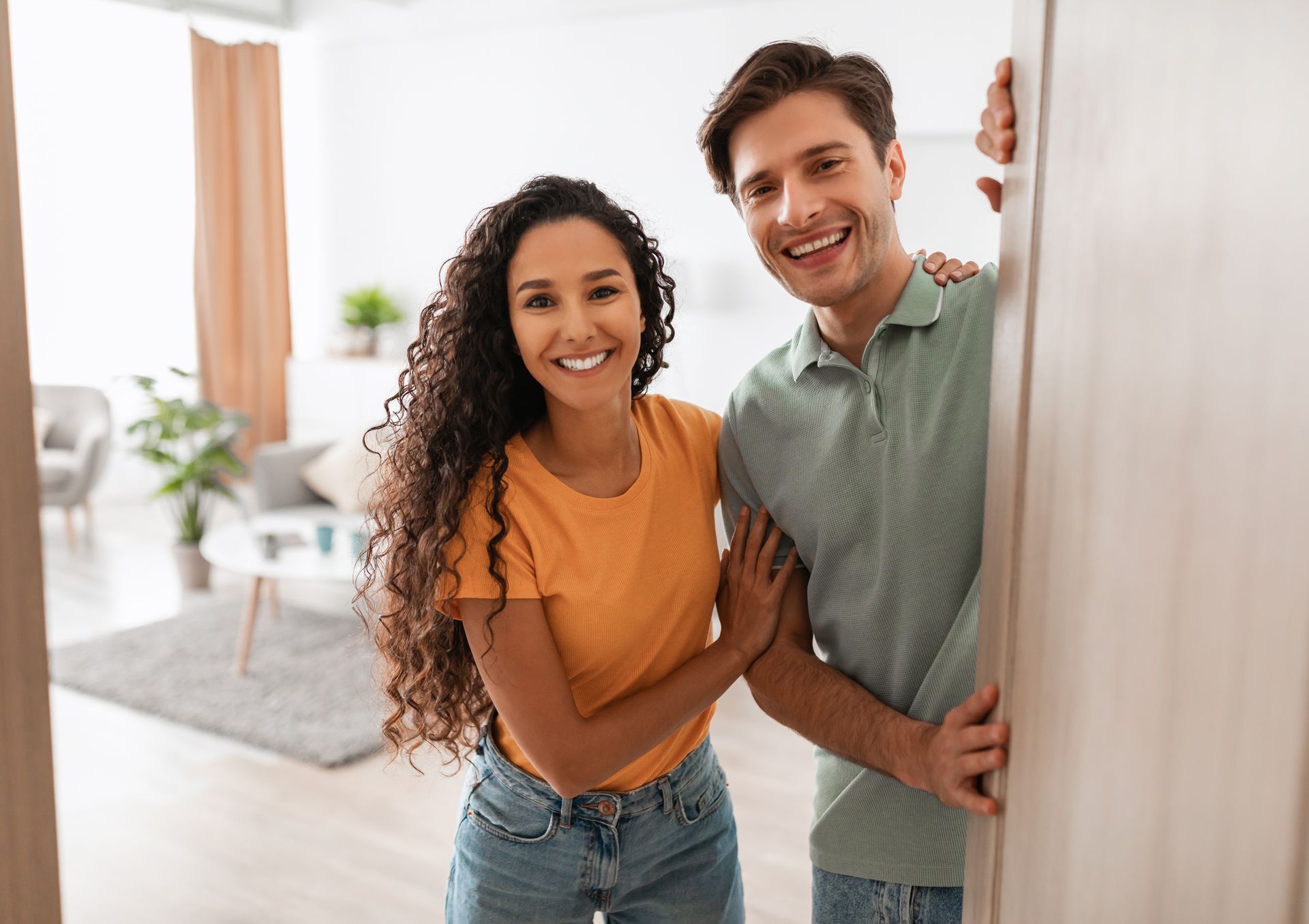 Smiling couple peeks from behind an open door in a bright living room