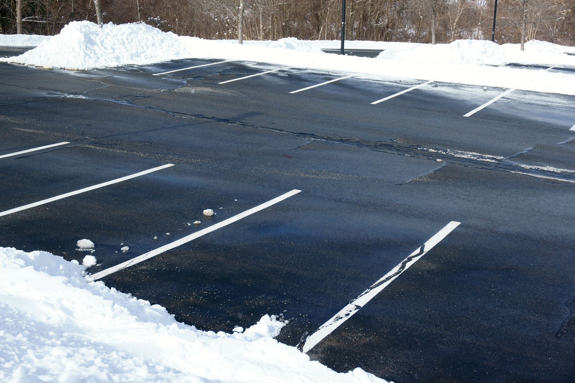 Snow-lined empty parking lot with dark asphalt and painted parking spaces