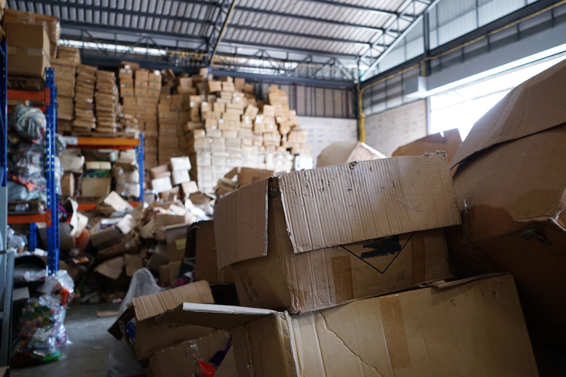 Warehouse filled with stacked cardboard boxes and packing materials under a metal roof