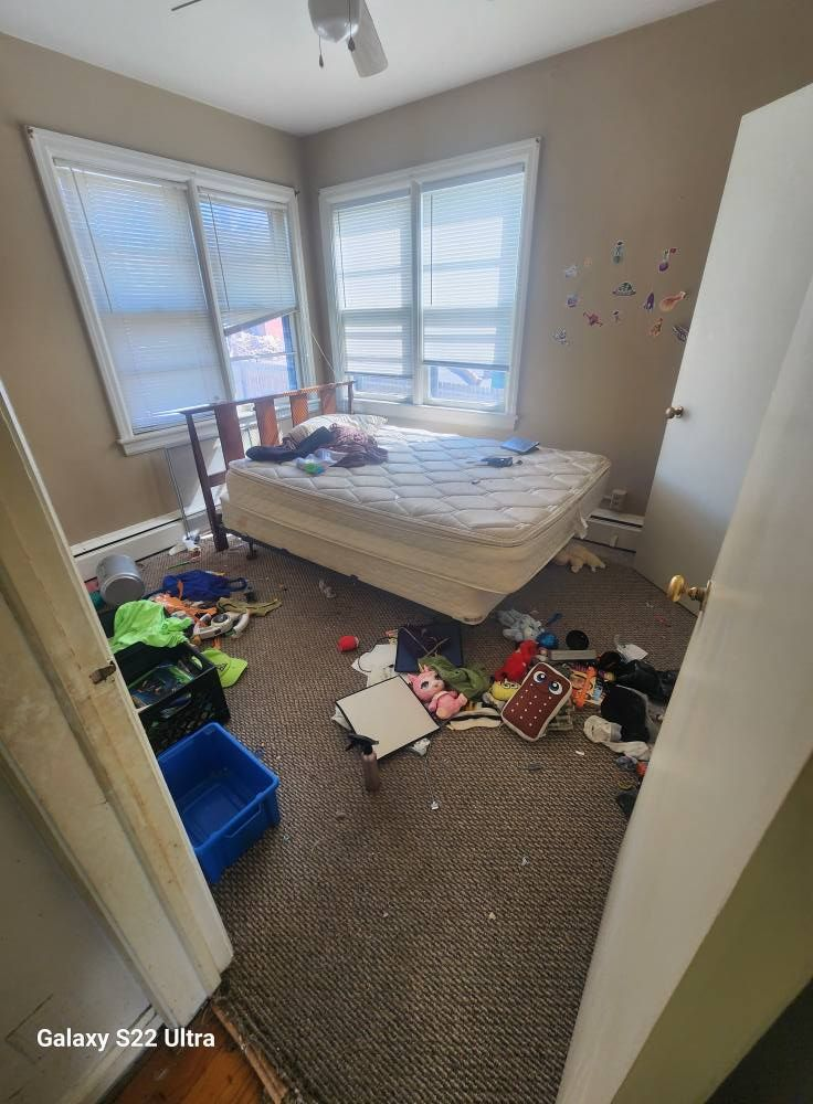 Messy bedroom with an unmade bed, scattered toys and clothes, and windows with blinds