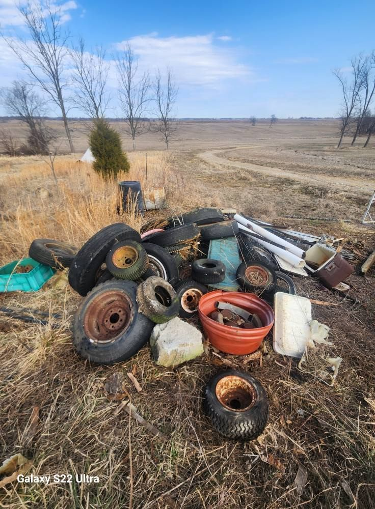 Pile of used tires, rims, and metal scraps scattered in a dry field under a blue sky.