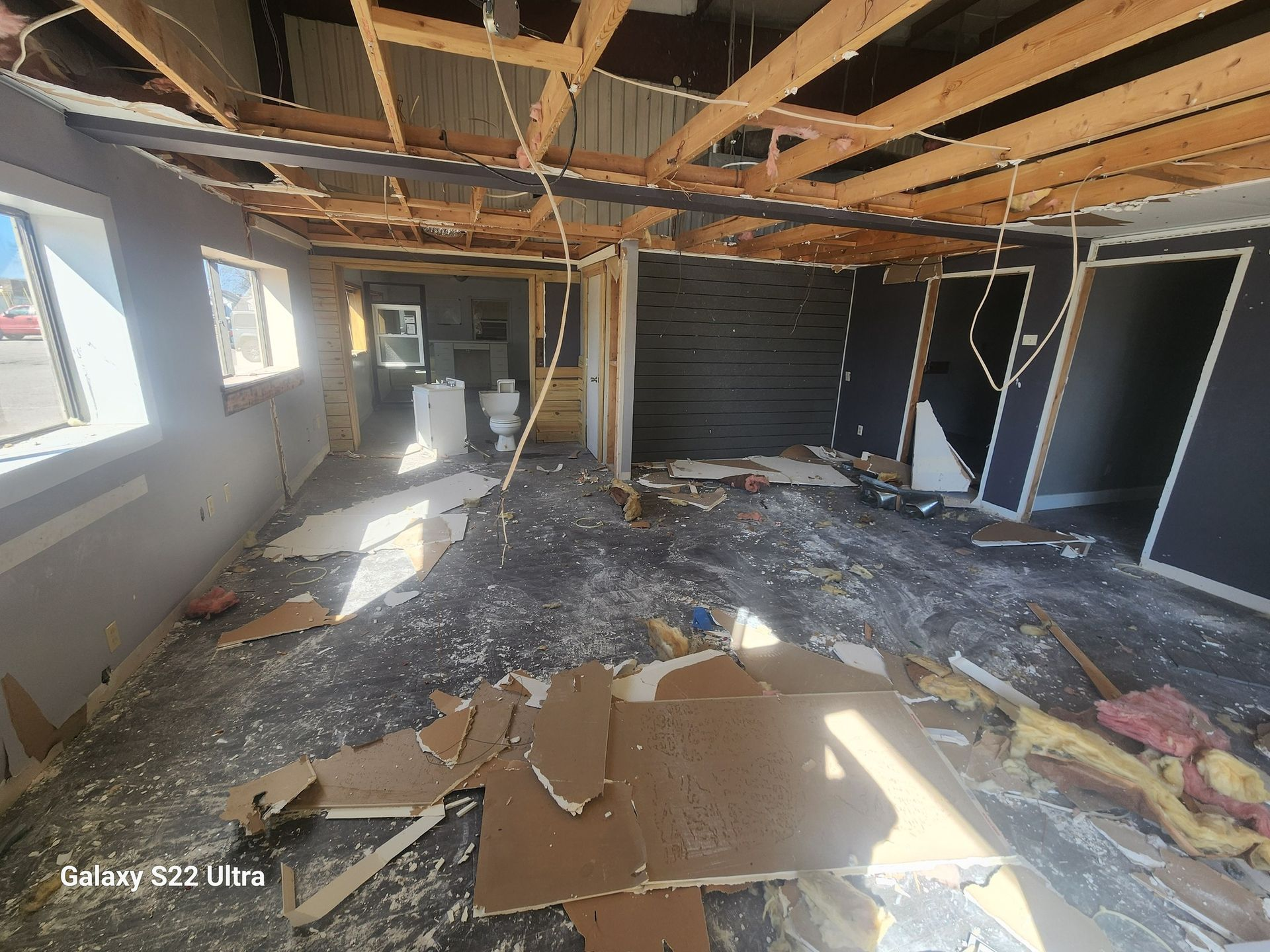 Damaged room with exposed ceiling beams, debris on floor, and broken walls after demolition