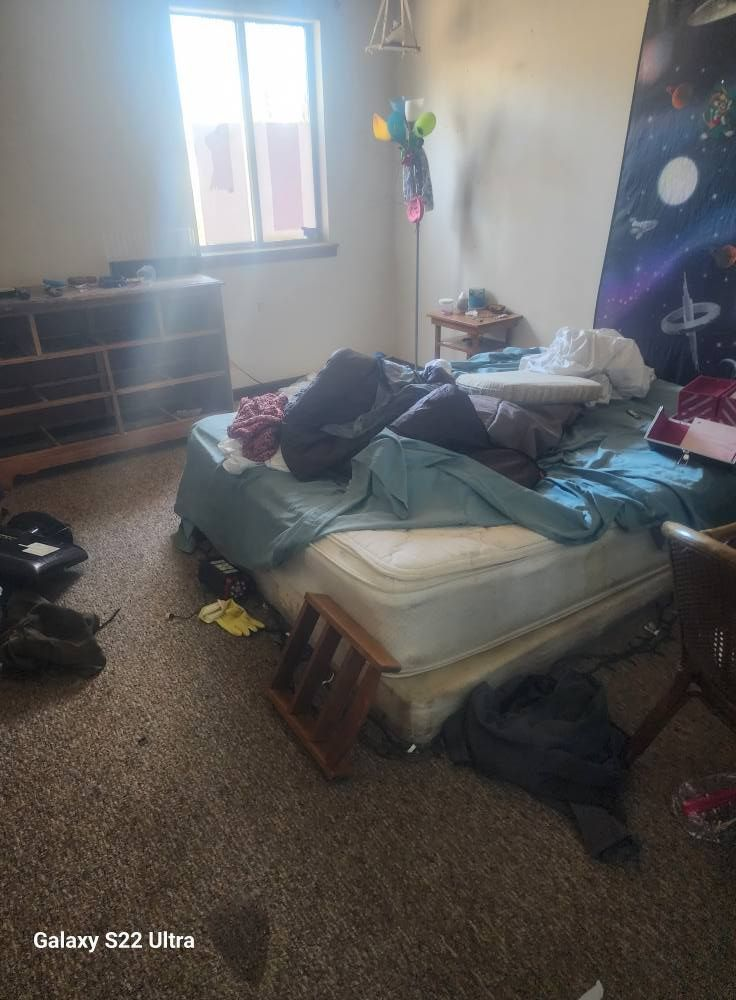 Cluttered bedroom with an unmade bed, scattered clothes, a window, and a colorful wall mural.