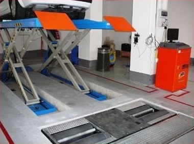 Auto su un ponte sollevatore nell'autofficina Milani per la convergenza delle ruote; ponte sollevatore arancione e blu, pavimento grigio.