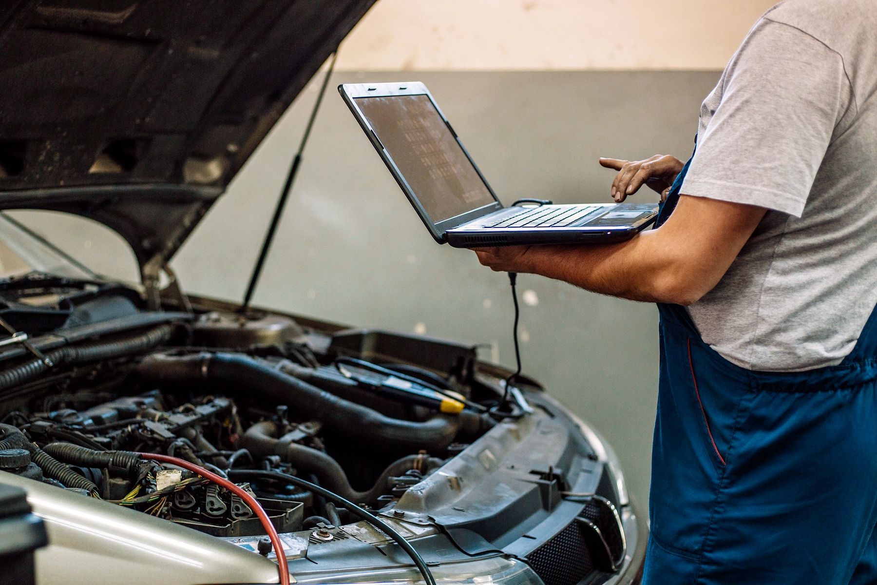 Meccanico che utilizza un computer portatile per diagnosticare il motore di un'auto in un'officina.