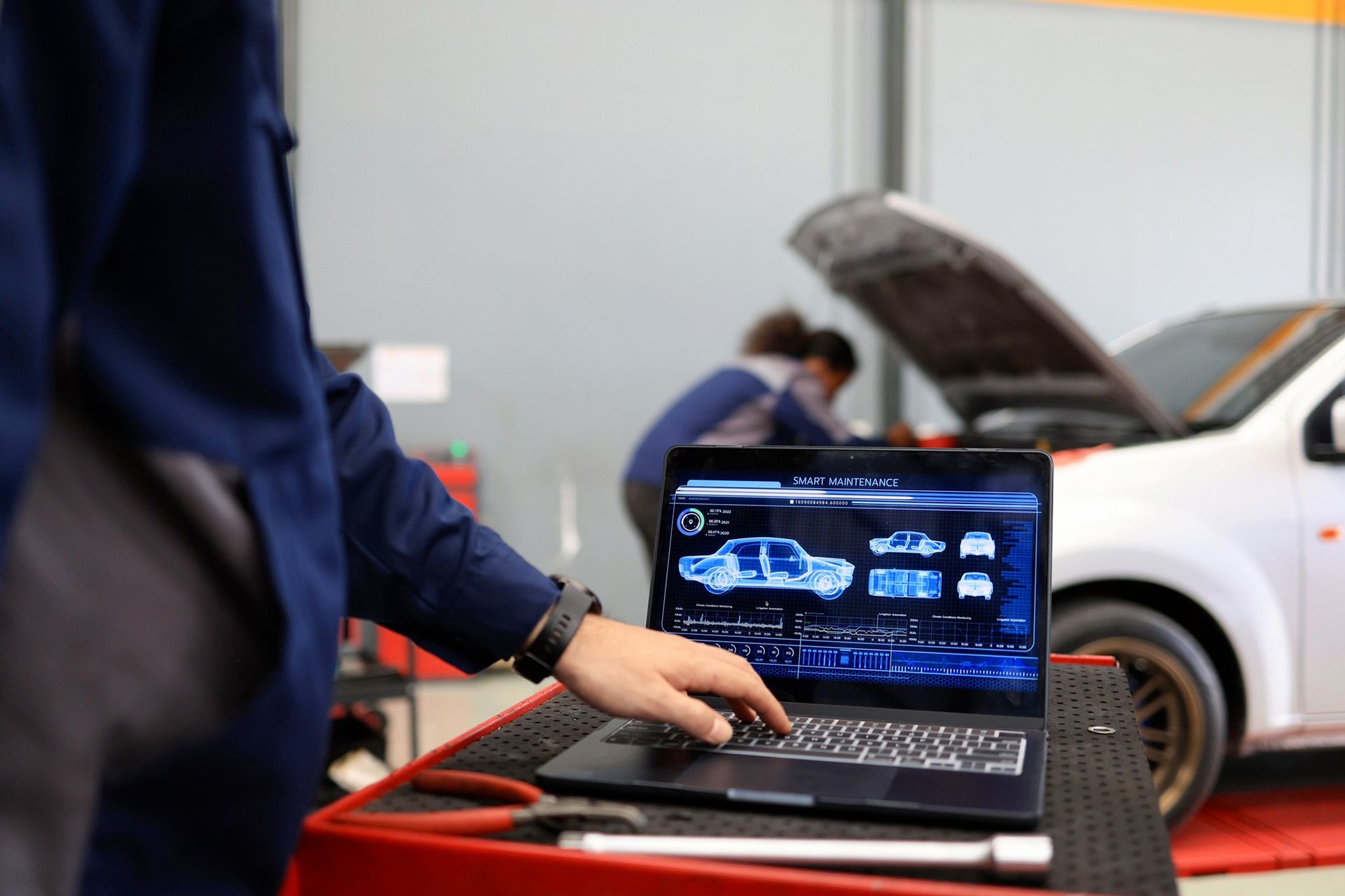 Il meccanico usa un computer portatile con la diagnostica dell'auto, mentre altri lavorano su un veicolo in un'officina.