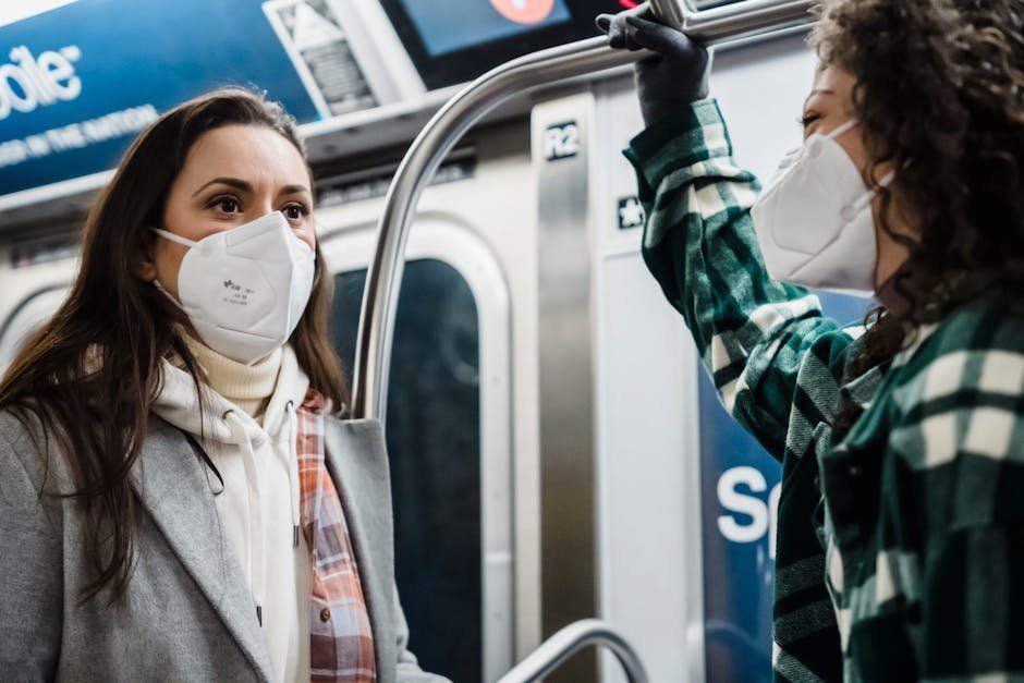Two women wearing face masks are riding a subway train.