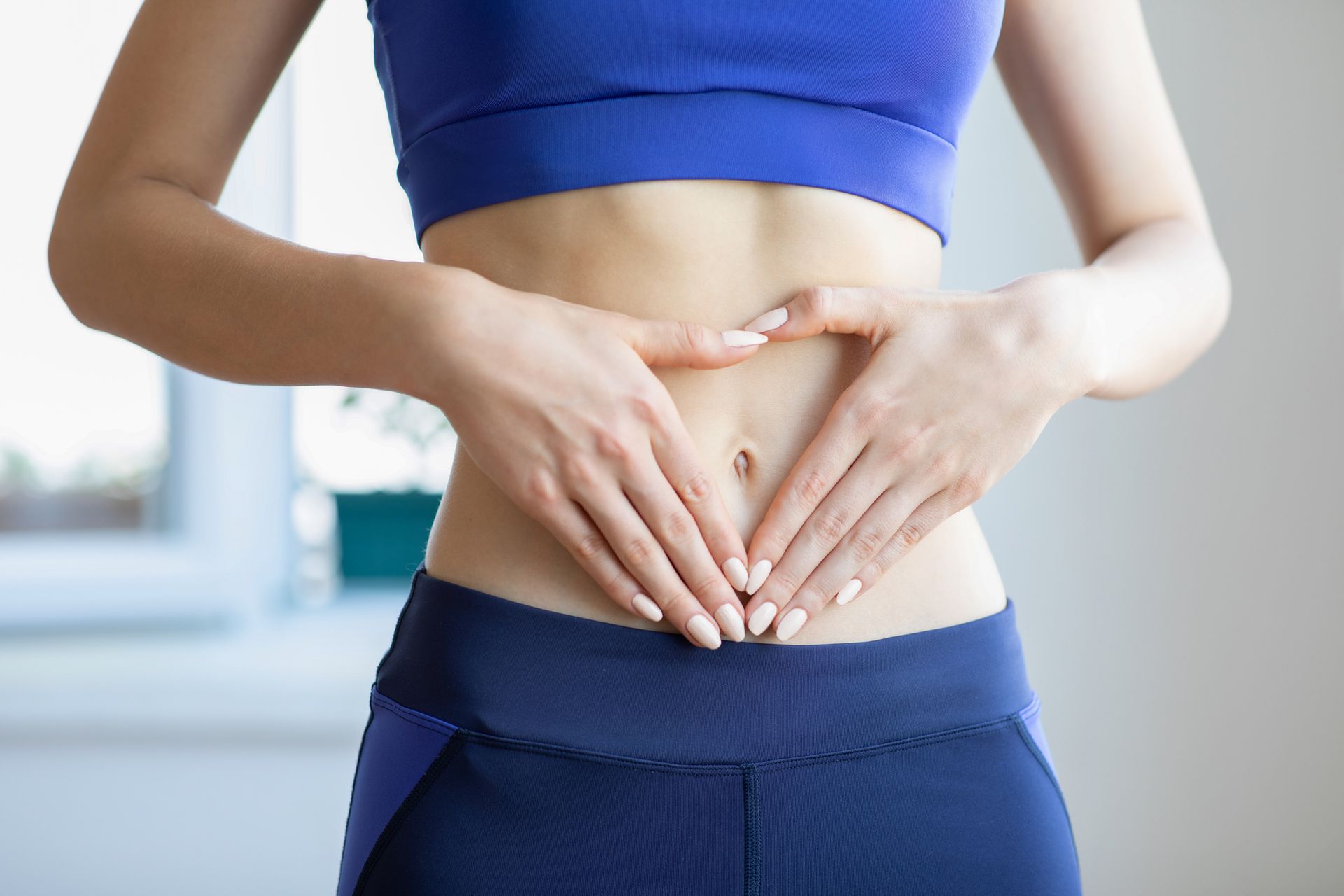 A woman is making a heart shape with her hands on her stomach.
