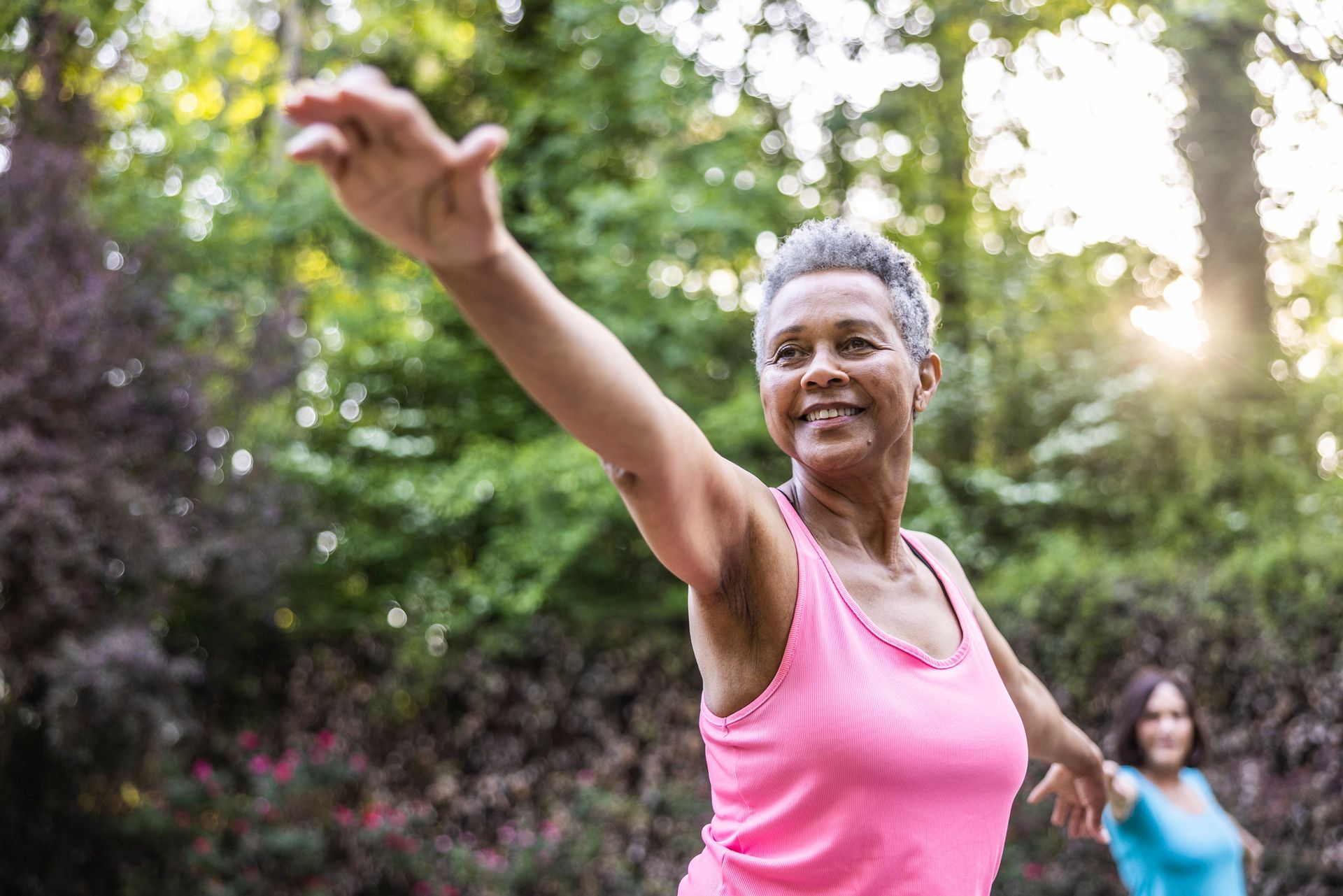 A woman in a pink tank top is stretching her arms in a park.