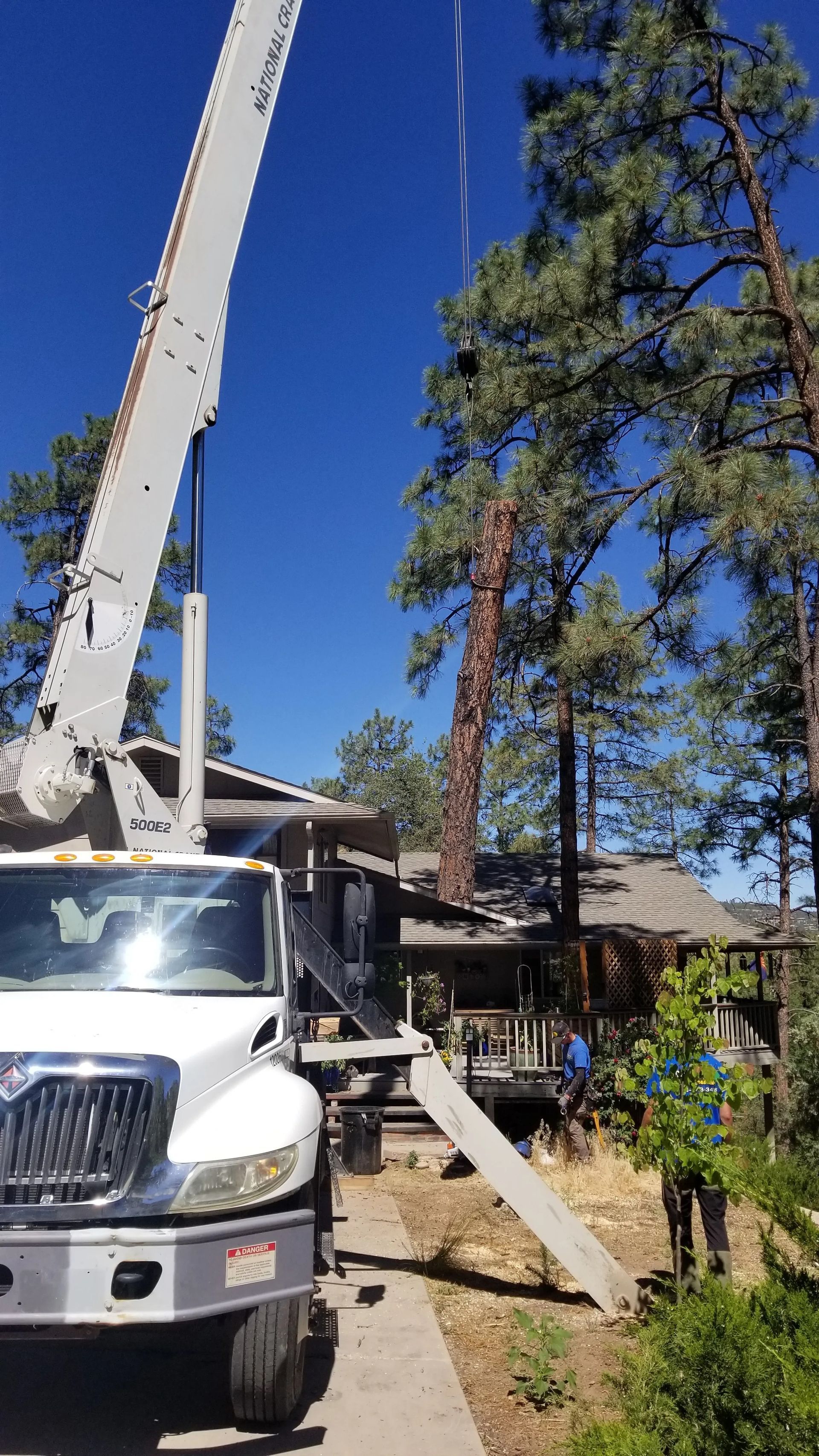 A white truck with a crane attached to it is parked in front of a house.