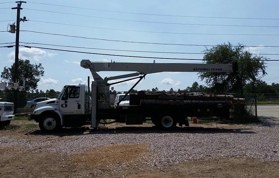A truck with a crane attached to it is parked in a gravel lot.