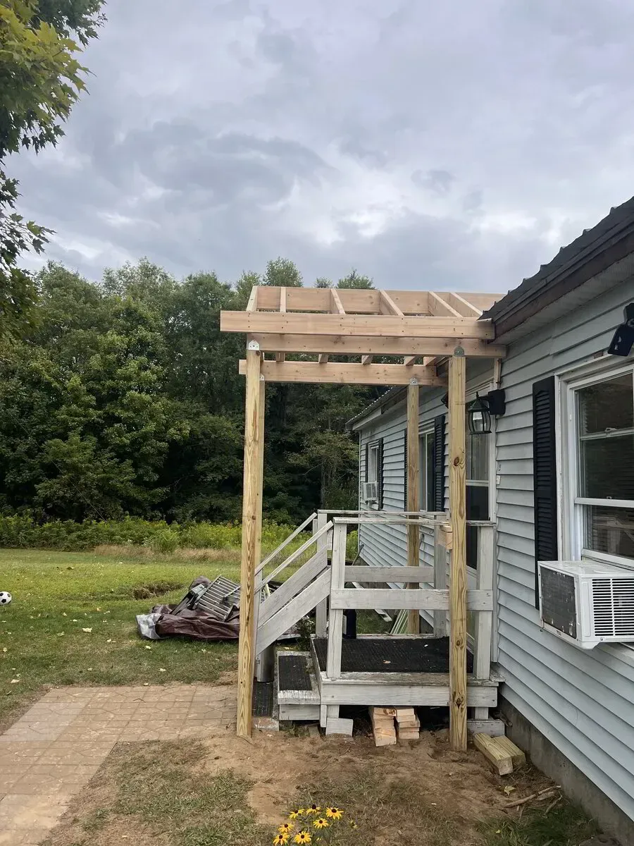 A newly built wooden porch frame attached to the side of a light blue house, overlooking a grassy yard.