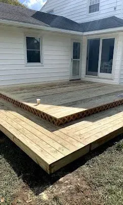 A two-level wooden deck attached to the back of a white house with sliding glass doors and lattice skirting.
