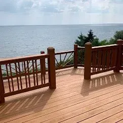 A wooden deck with railing overlooking a calm, expansive lake under a cloudy sky.