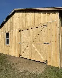 A rustic wooden barn exterior featuring board and batten siding, a window, and large double doors with diagonal bracing.