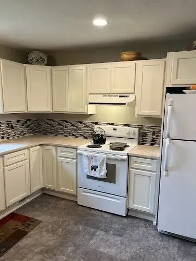 A kitchen with cream cabinets, a white stove, a white refrigerator, and a grey mosaic tile backsplash.