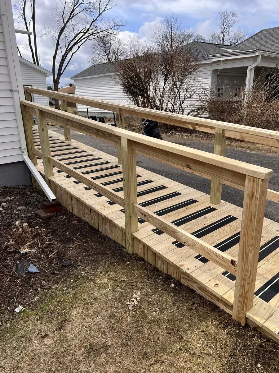 A wooden ramp with black anti-slip strips and handrails leading up to the side entrance of a residential home.
