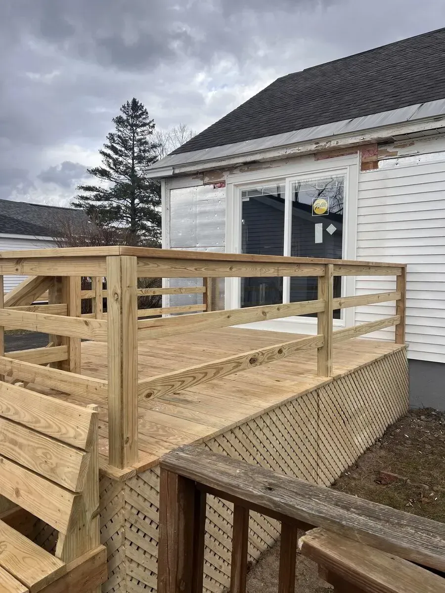A newly constructed wooden deck featuring railings and lattice skirting stands outside a house with white siding.