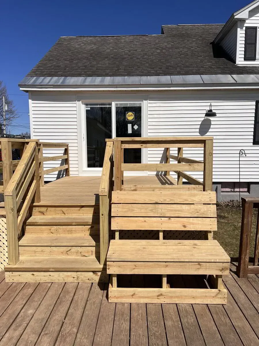 Wooden steps and a matching bench on a sunny deck attached to a white house with horizontal siding.