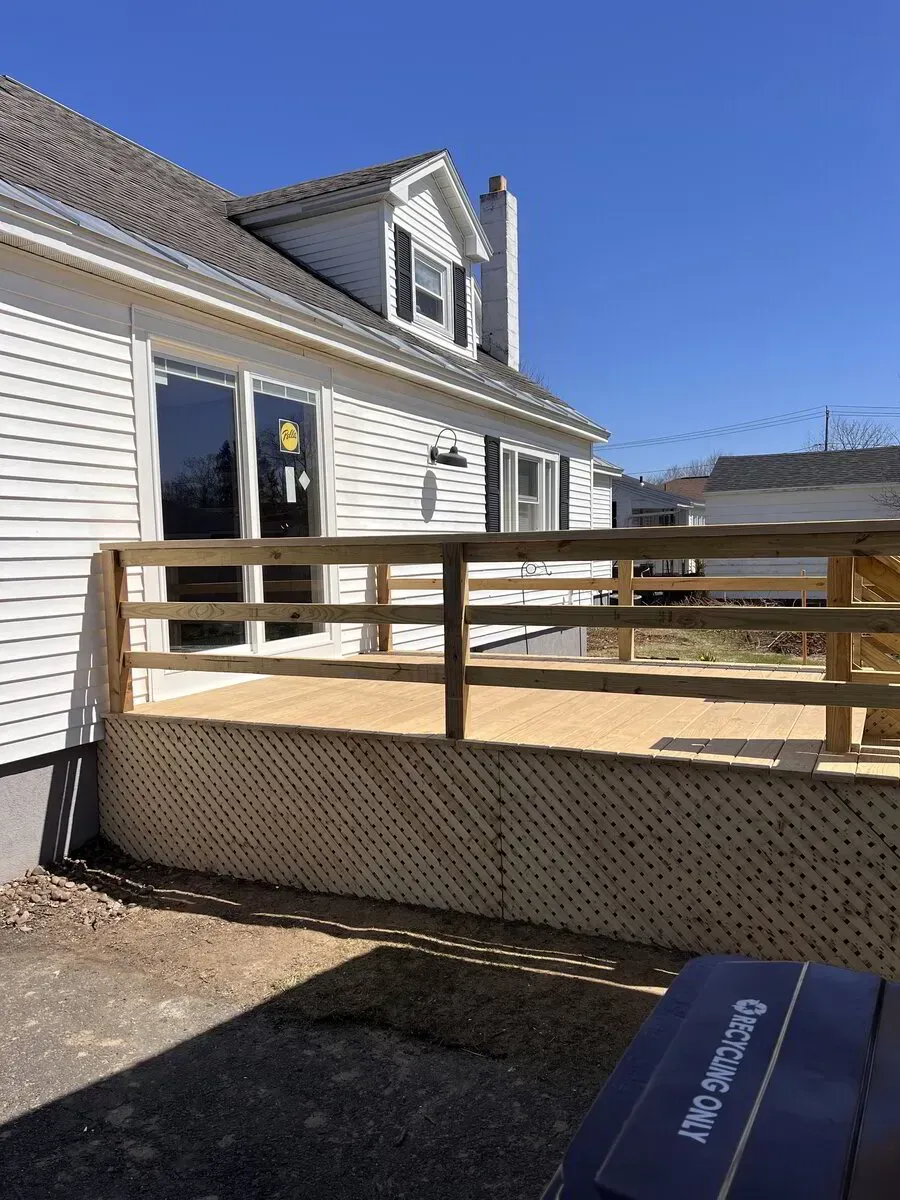 A newly constructed wooden deck with railings and lattice skirting attached to the side of a white house.