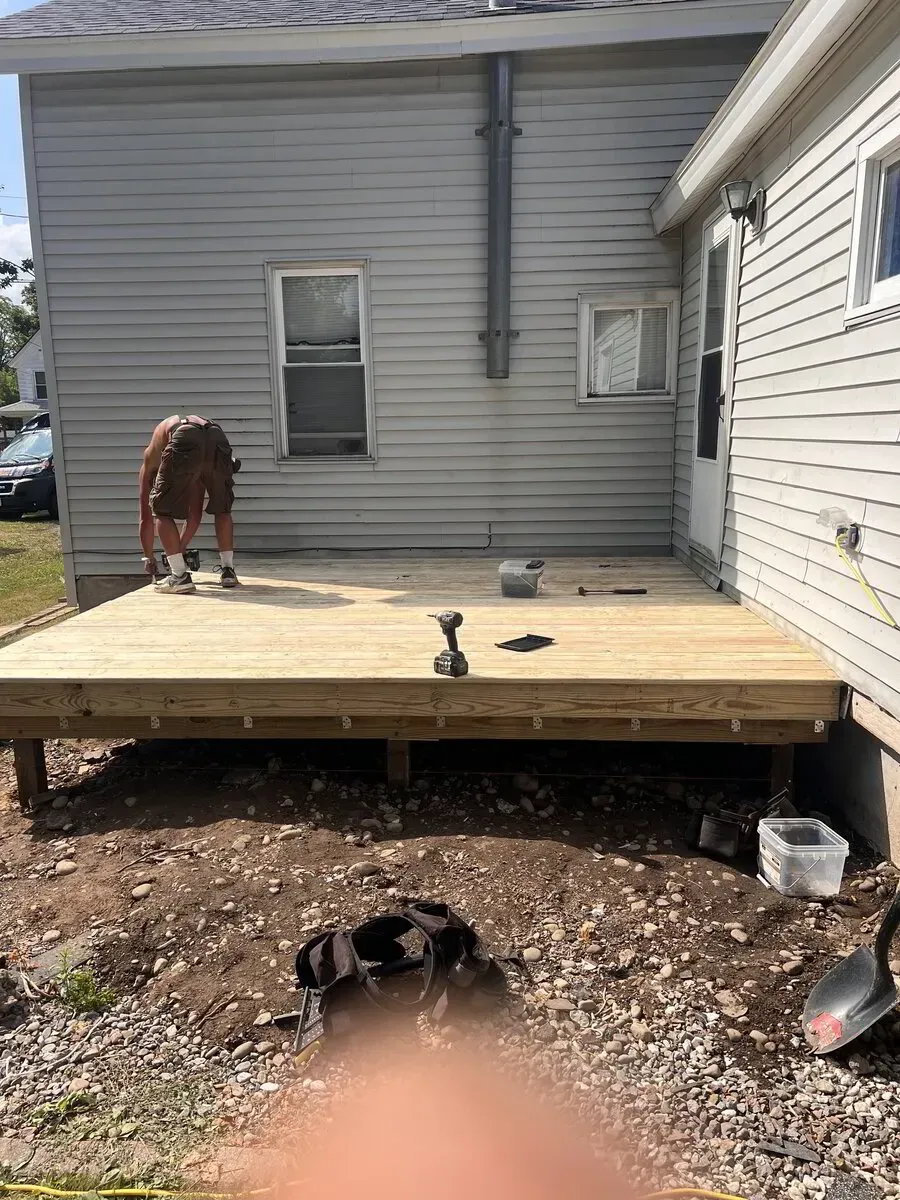 A person working on a newly built wooden deck attached to the side of a light-gray house.