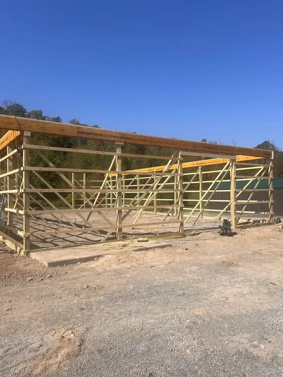 The wooden frame of a building under construction on a gravel lot under a clear blue sky.