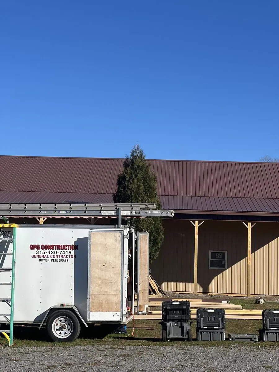 A construction trailer sits in front of a metal-sided building under a bright blue sky.