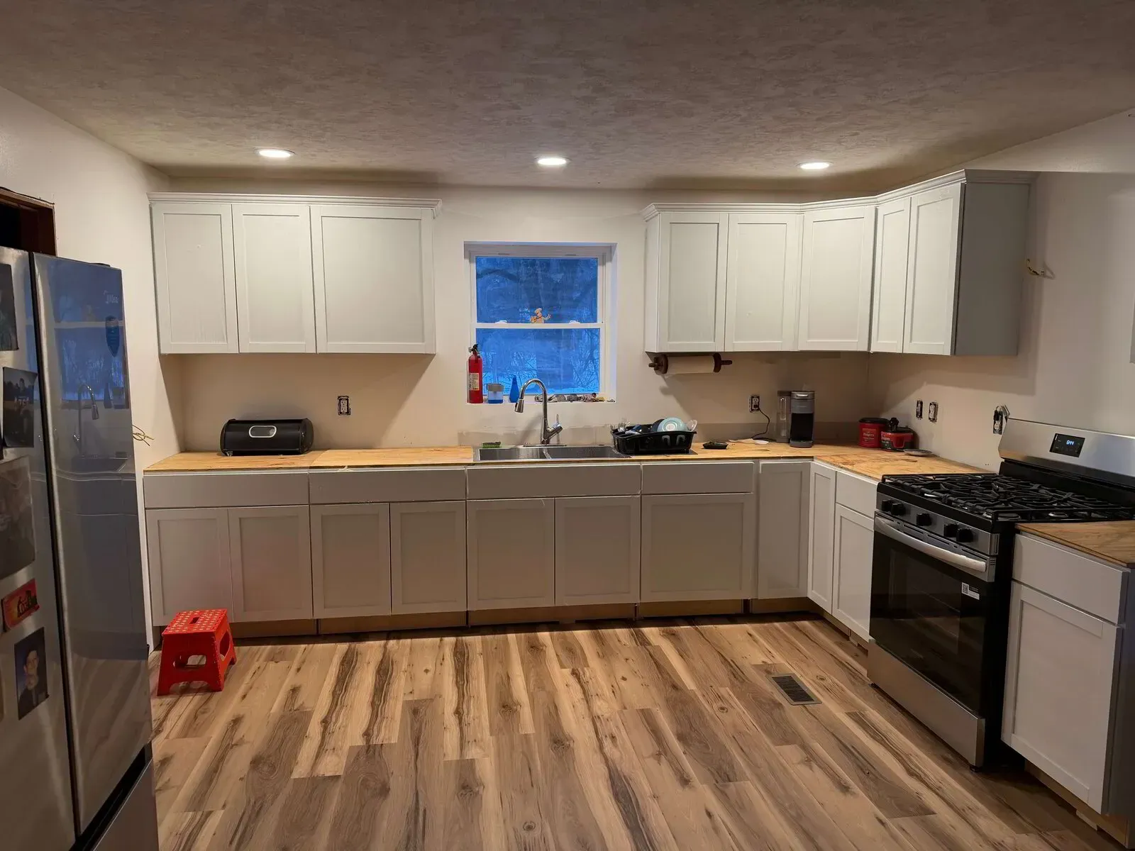 A modern kitchen with white cabinets, light wood-look flooring, butcher block countertops, and a stainless steel stove.