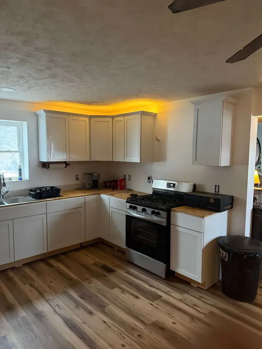 A kitchen with white cabinets, wood-look flooring, a gas stove, and warm under-cabinet LED strip lighting.