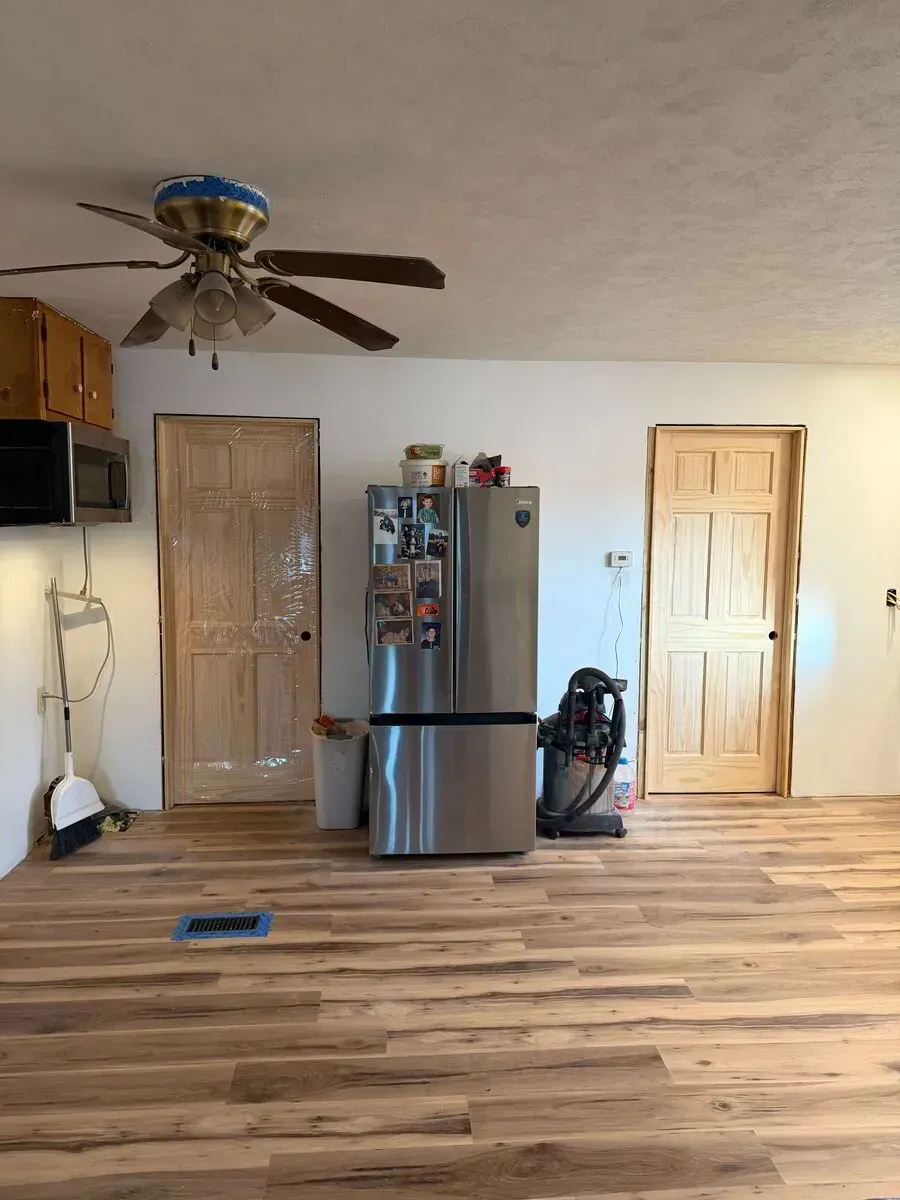 A kitchen area with a ceiling fan, light wood floors, a stainless steel refrigerator, and two wood doors.