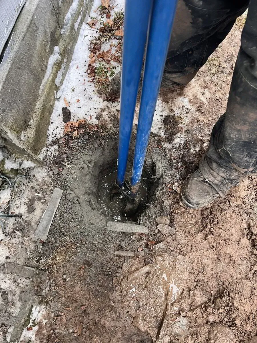 A pair of blue poles are being set into a hole in the dirt, anchored by wet concrete next to a foundation.