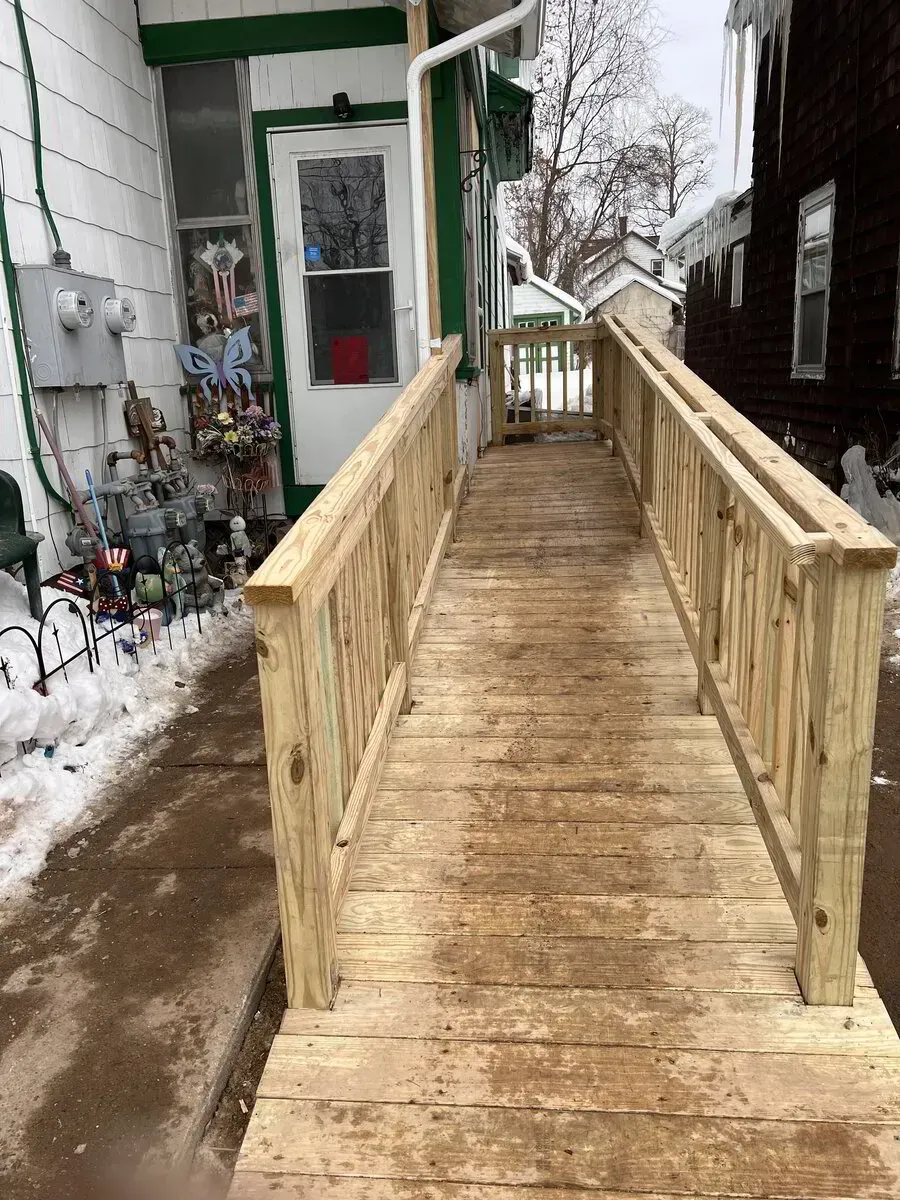 A newly built wooden wheelchair ramp leading up to a house entrance covered in snow.
