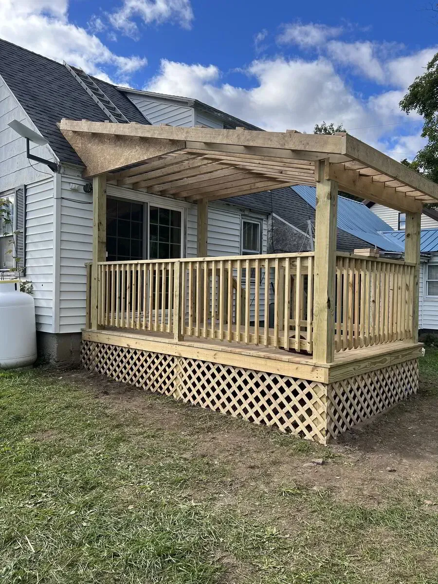 A wooden deck with a partially covered pergola and lattice skirting attached to the side of a white house.