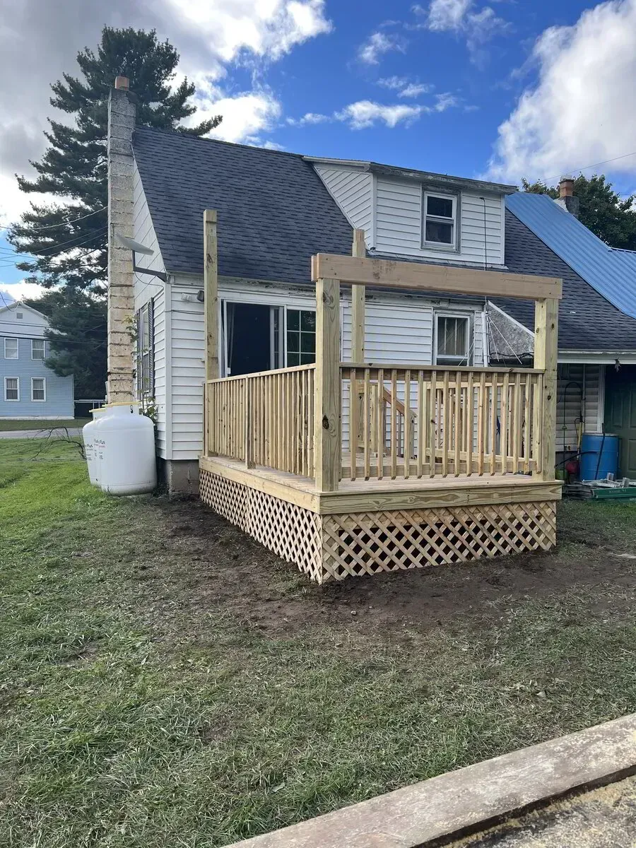 A partially constructed wooden deck with lattice skirting and vertical framing posts attached to the side of a white house.