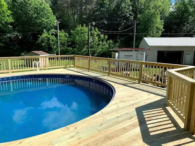 A circular above-ground swimming pool with blue water surrounded by a newly built wooden deck and railing.