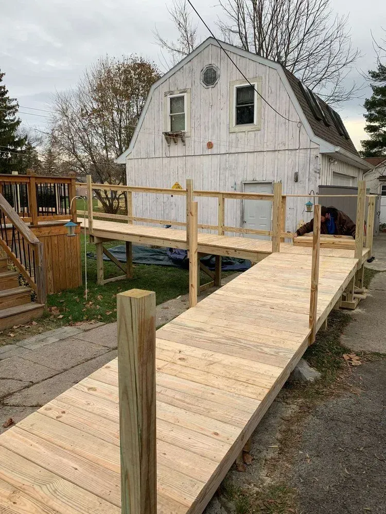 A newly constructed wooden wheelchair ramp leading up to a raised deck in front of a white barn-style garage.