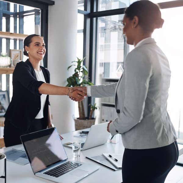 An accountant and her client shake hands in a bright office meeting room.