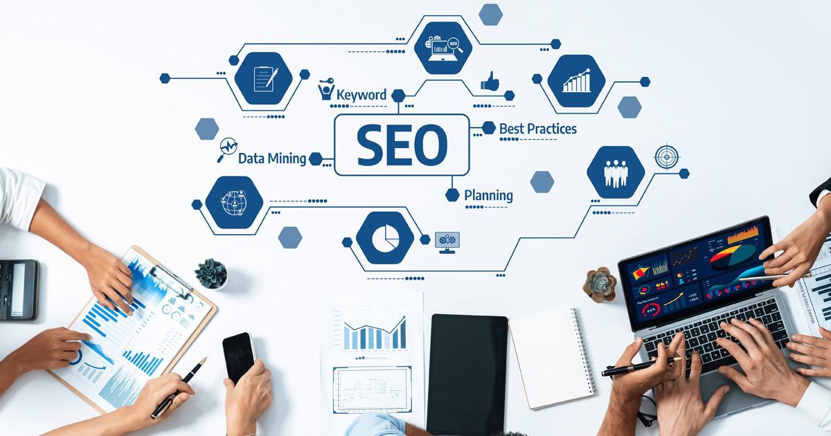 SEO Long Island by Solution Web Designs. A top-down view of people working around a desk with SEO icons and diagrams surrounding a central SEO label.