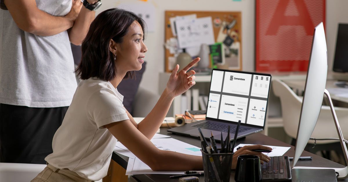 A person points at a laptop screen displaying a grid layout, collaborating with a colleague in a bright, creative office doing a Website Redesign Services at Solution Web Designs