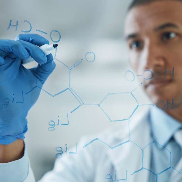 Chemical Engineer in lab coat and gloves drawing a chemical structure on glass with a marker.