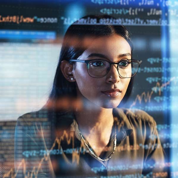 Female Software Engineer with glasses, focused on a computer screen displaying code and graphs. Low-lit room.