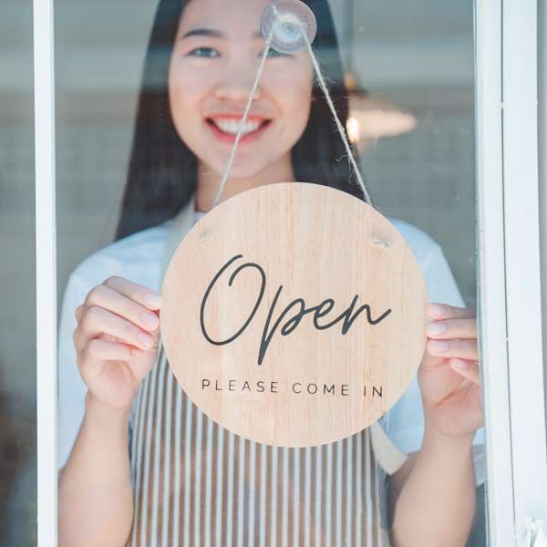 small business owner smiling behind a glass door, holding an