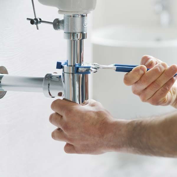 Plumber using a wrench to tighten a chrome pipe under a sink.