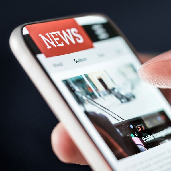 Press Releases showing a close-up of a smartphone displaying a news website, held by a person. Red 