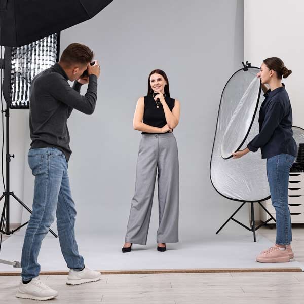 A photographer captures a portrait of a professional model in a studio, while an assistant holds a reflector to add light.
